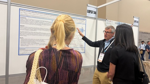 professor Roger Barker talking through a poster to 2 individuals at a conference.   